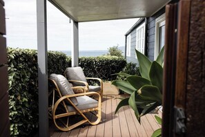 A covered outdoor area with a wicker chair, a potted plant, and a view of the sea. - Sea Cliff Sands Gerroa (Gerroa)