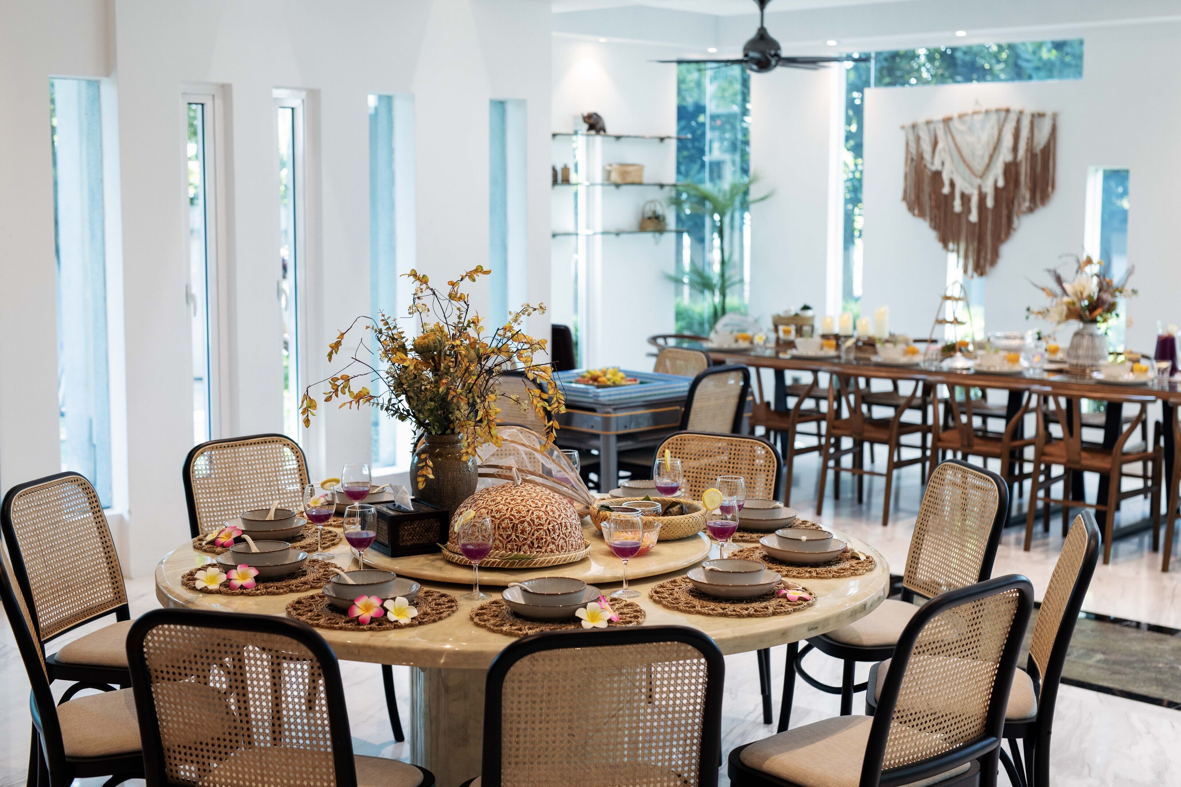 Un comedor con mesas redondas, sillas de mimbre y un jarrón decorativo en el centro.