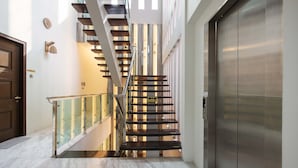 A modern interior with a staircase, a glass railing, and a closed elevator. - 25000sqft Grand Luxe Villa PJ 13BR 42Pax (Petaling Jaya)
