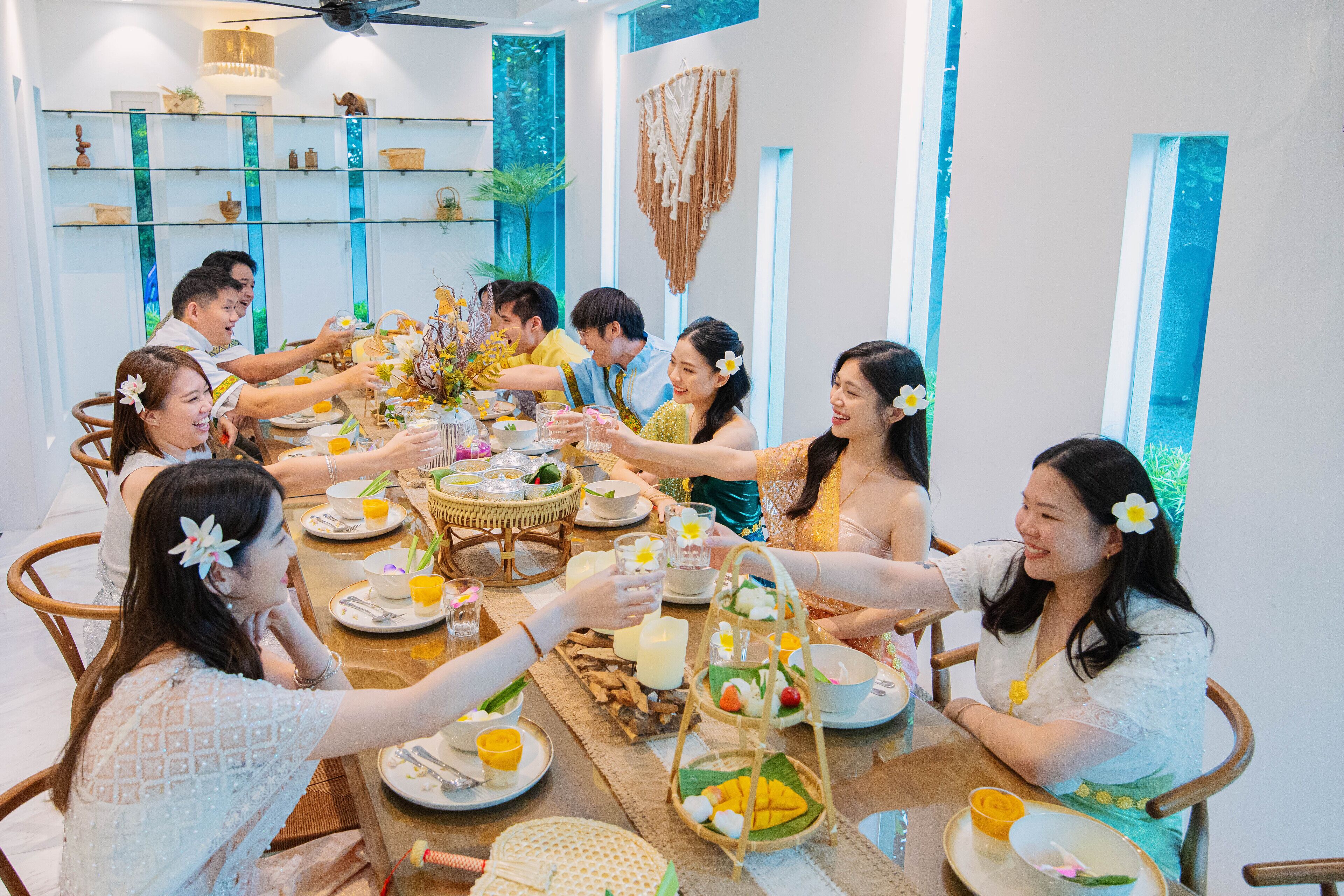 A group of people seated around a table with various dishes and drinks, in a room with shelves and decorative items.