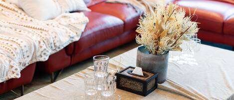 Una habitación con un sofá de cuero rojo, una mesa con un jarrón de flores secas y varios vasos.