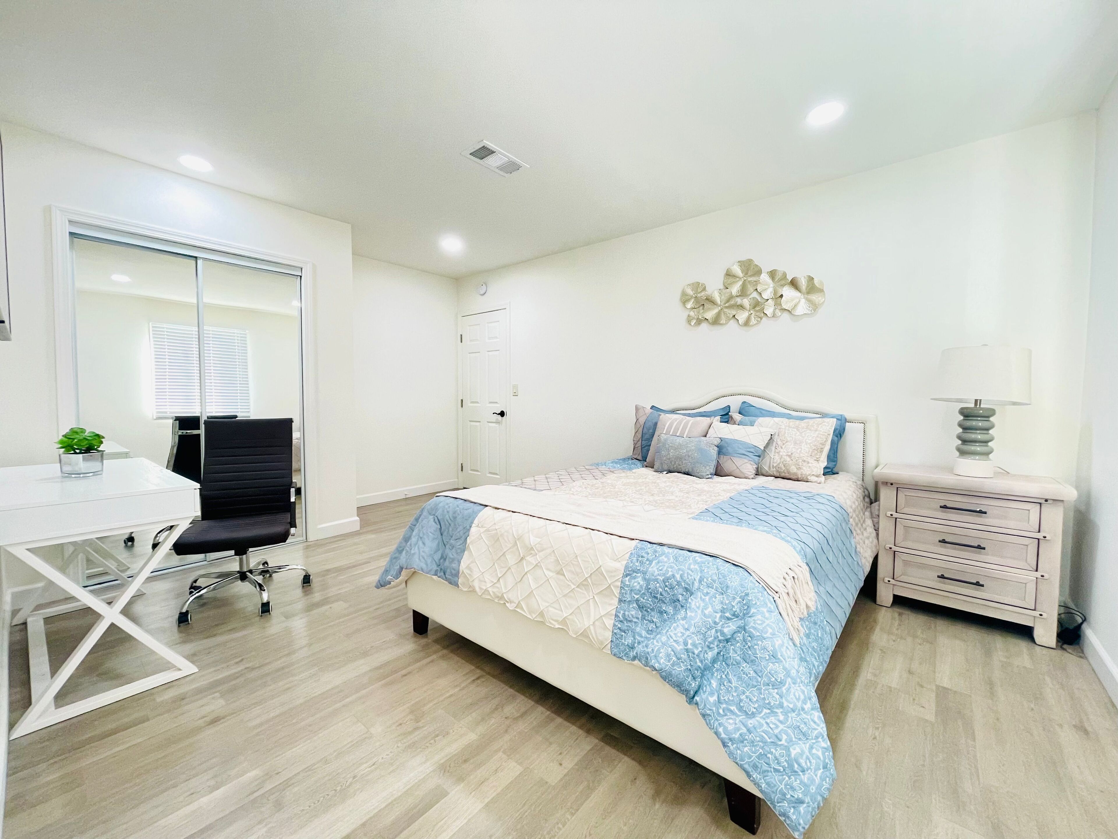 Un dormitorio con cama, mesita de noche, lámpara y un escritorio con silla.