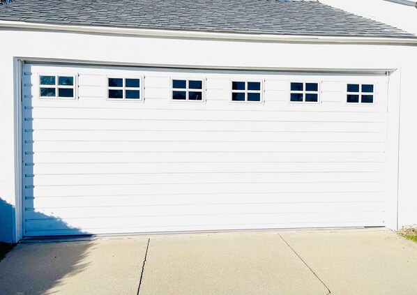 A white garage door with four windows and a concrete driveway.