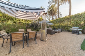 An outdoor patio with striped umbrellas, a grill, and seating. - The Beach House (Montecito)