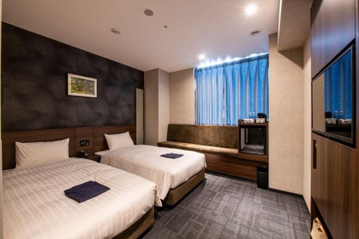 A hotel room with two beds, a small seating area, a television, and a window with curtains.