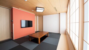 A room with a television mounted on a red wall, a wooden table, tatami mats on the floor, and large windows on one side. - Welina Premier Osaka Namba (Osaka)
