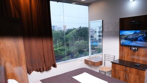 Ein Hotelzimmer mit einem großen Bett, einer Holzkommode, einem Fernseher und einem Fenster mit Blick auf Gebäude und Bäume.