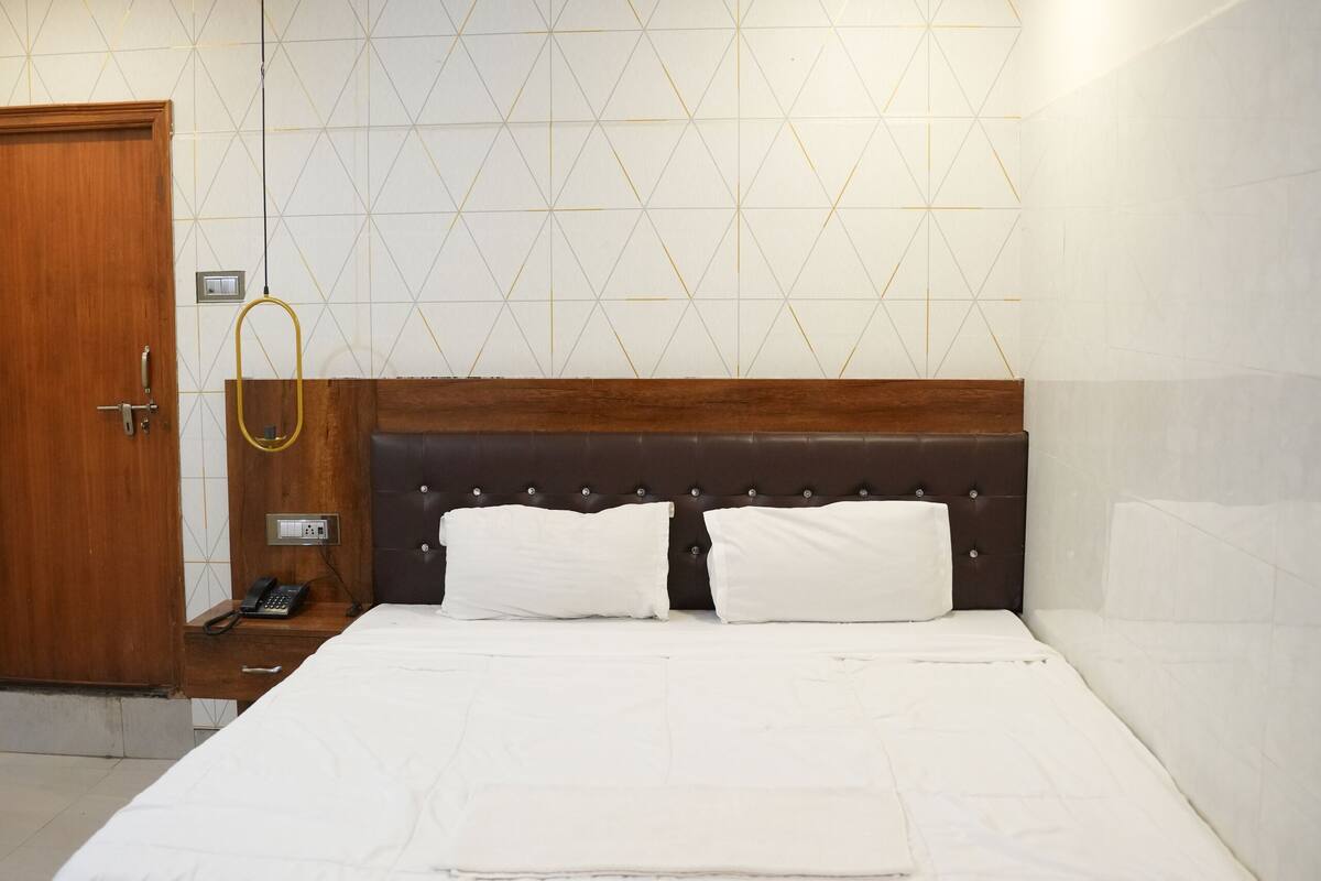 Habitació d'hotel moderna amb un llit de fusta, roba de llit blanca i un mur amb un disseny geomètric.