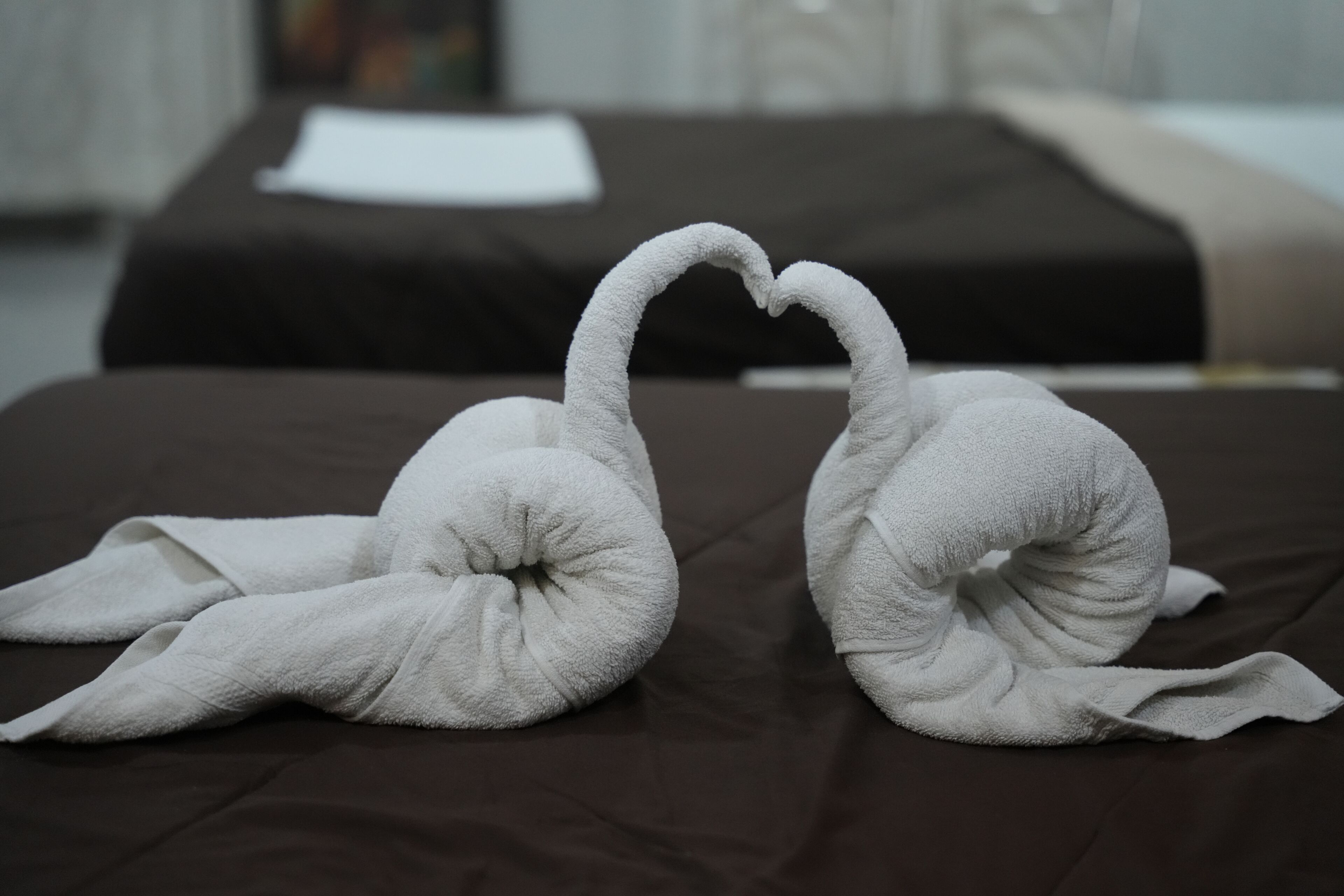 Two towels arranged in the shape of swans on a bed with a brown cover.
