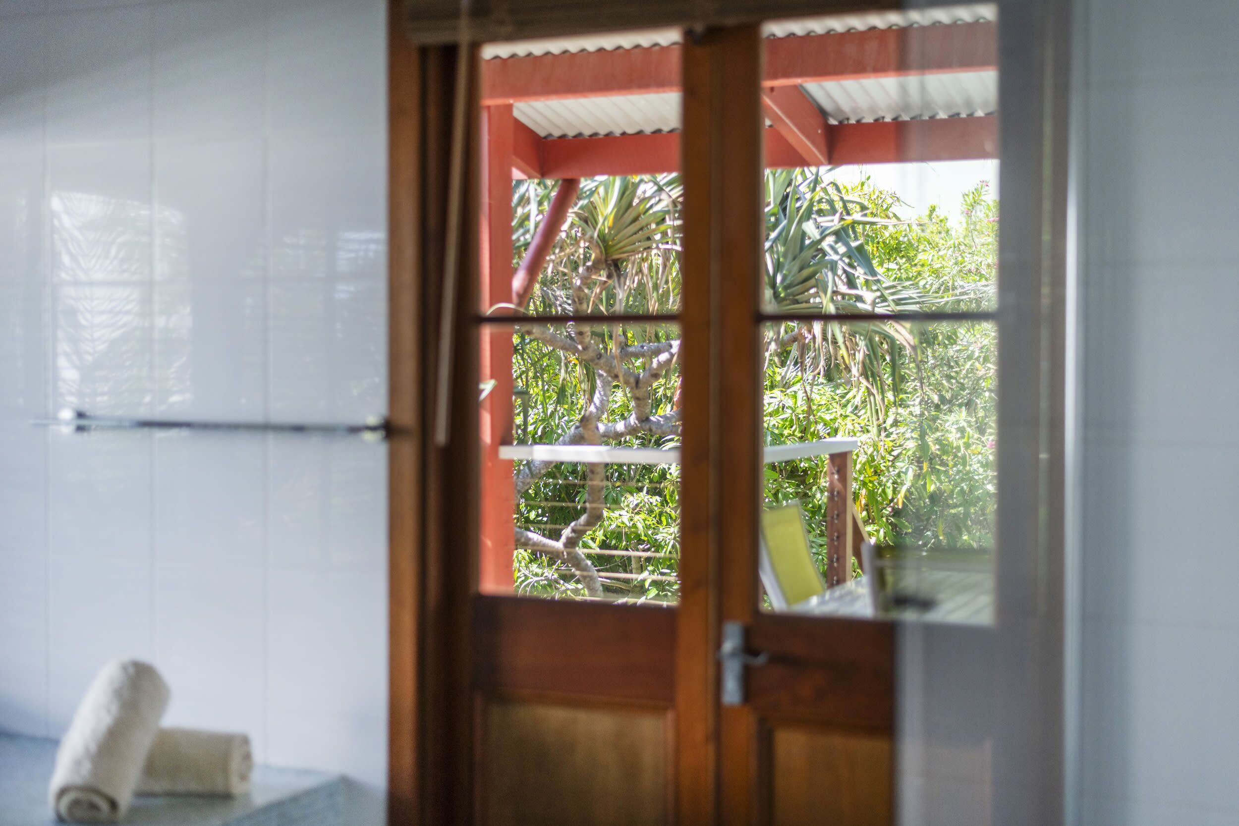 Un baño con puerta de madera que da a un balcón con vistas a zonas verdes.