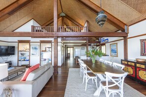 Un vaste espace de vie de style loft, doté d’un haut plafond, de poutres en bois, d’une table à manger avec des chaises, d’un canapé et d’un téléviseur.