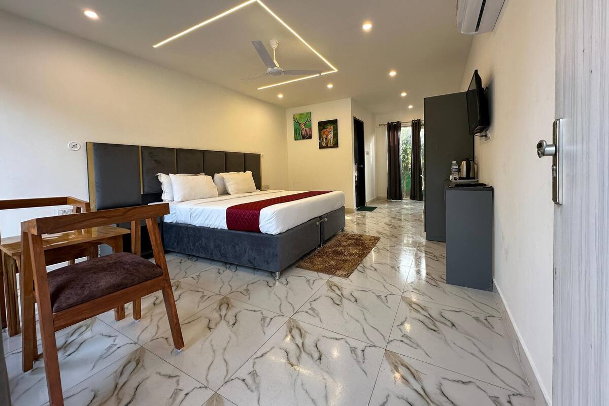 Une chambre d’hôtel moderne avec un grand lit, une chaise en bois, un bureau et un téléviseur fixé au mur.