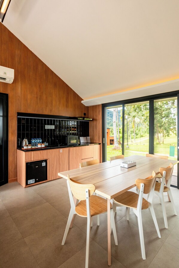 Una cocina moderna con encimera de madera, microondas integrado y refrigerador. Hay una mesa de comedor con seis sillas.