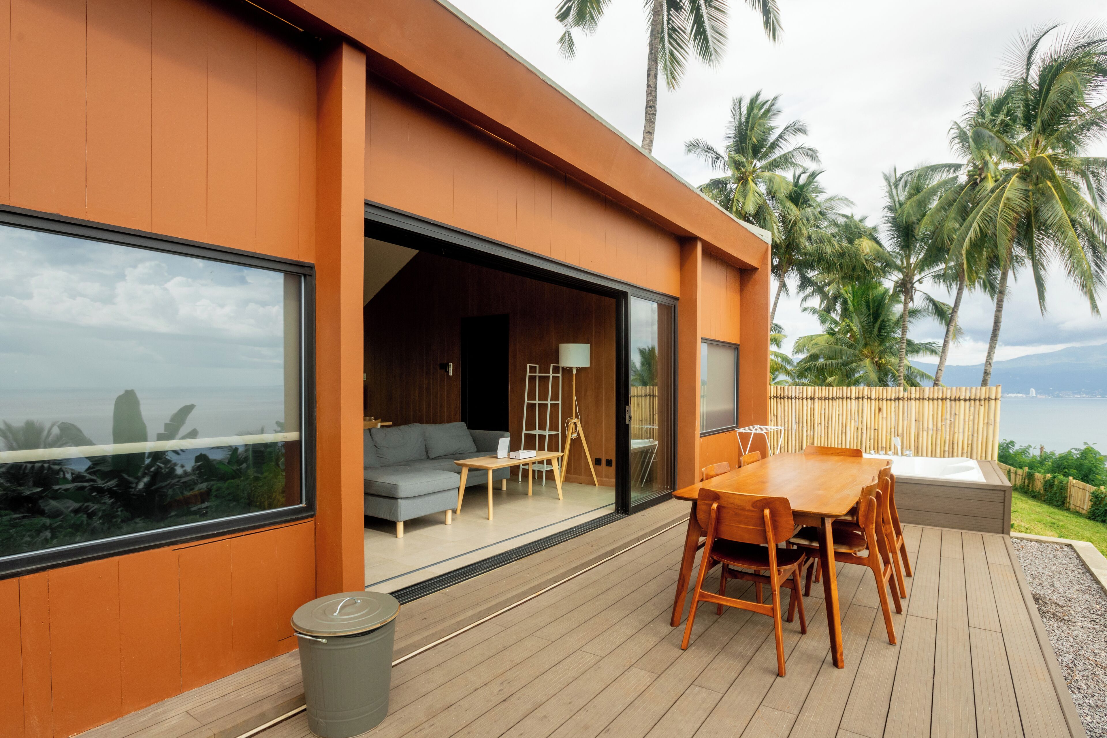 A modern house with a wooden deck, a dining area, and a large window overlooking the ocean.