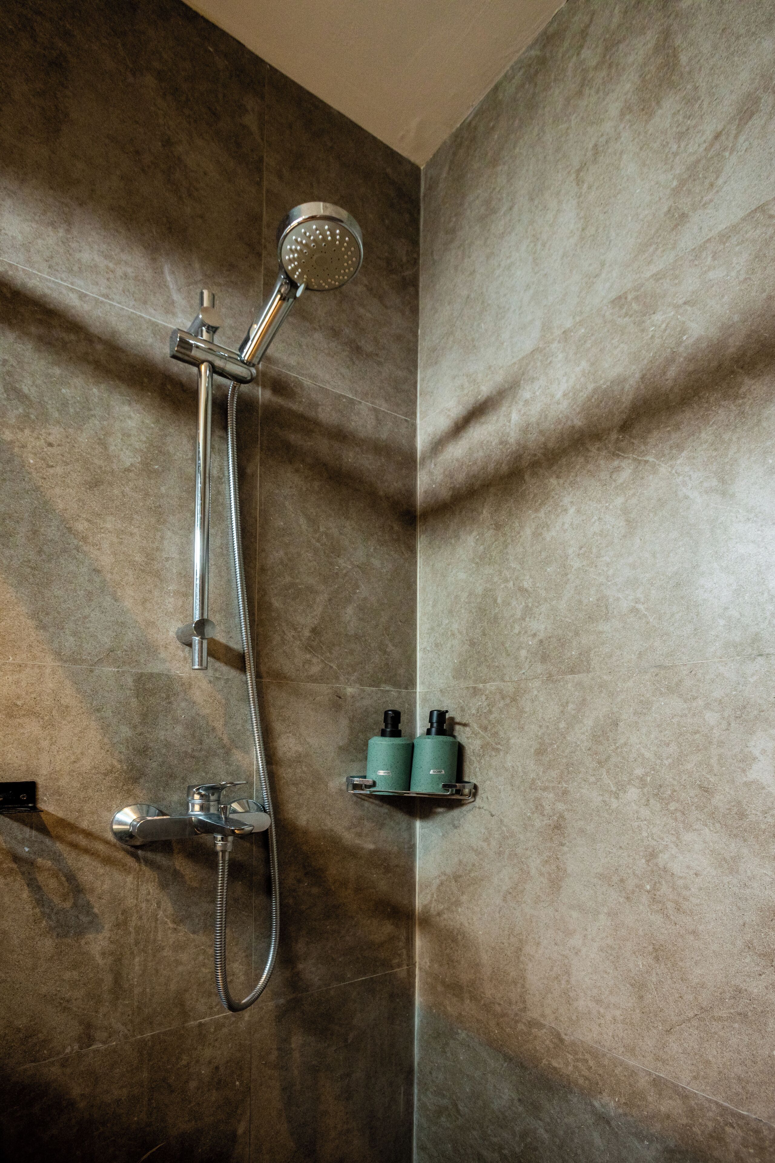 A shower with a handheld showerhead and a wall-mounted faucet.
