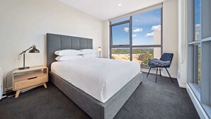 Een moderne slaapkamer met een groot bed, een nachtkastje, een stoel en uitzicht op een bouwplaats door het raam.