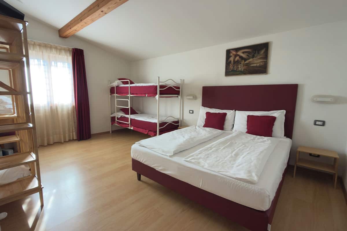 Une chambre d’hôtel avec un grand lit, une armoire en bois, un lit superposé et un tableau au mur.