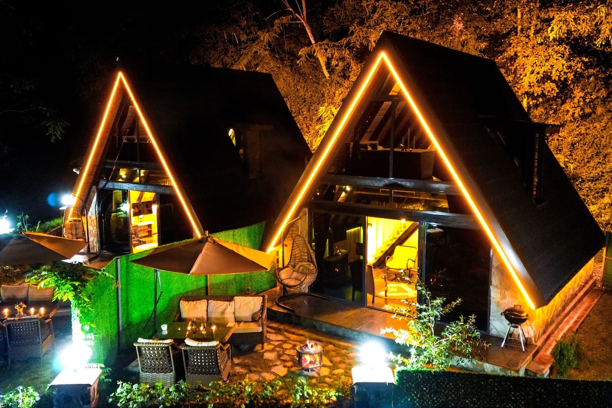 A modern, triangular-shaped house with a patio area featuring outdoor furniture and a barbecue.