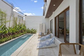 A modern outdoor pool area with a clear blue pool, lounge chairs, and a small table. - Roselle Villa by Betterplace (Kerobokan)