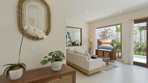 Una sala de estar moderna con un sofá, un espejo grande y un televisor. Hay plantas en macetas y un aparador de madera.