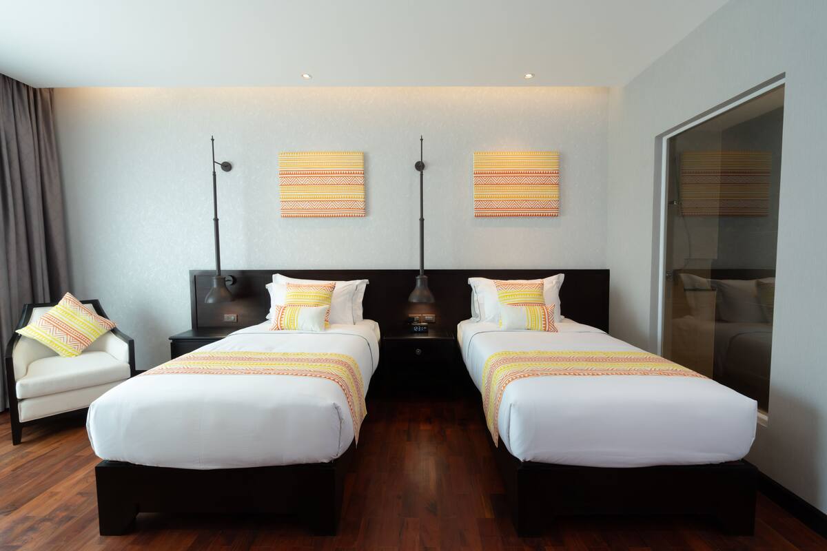 Une chambre d’hôtel avec deux lits, une chaise, une table de chevet et une grande fenêtre.