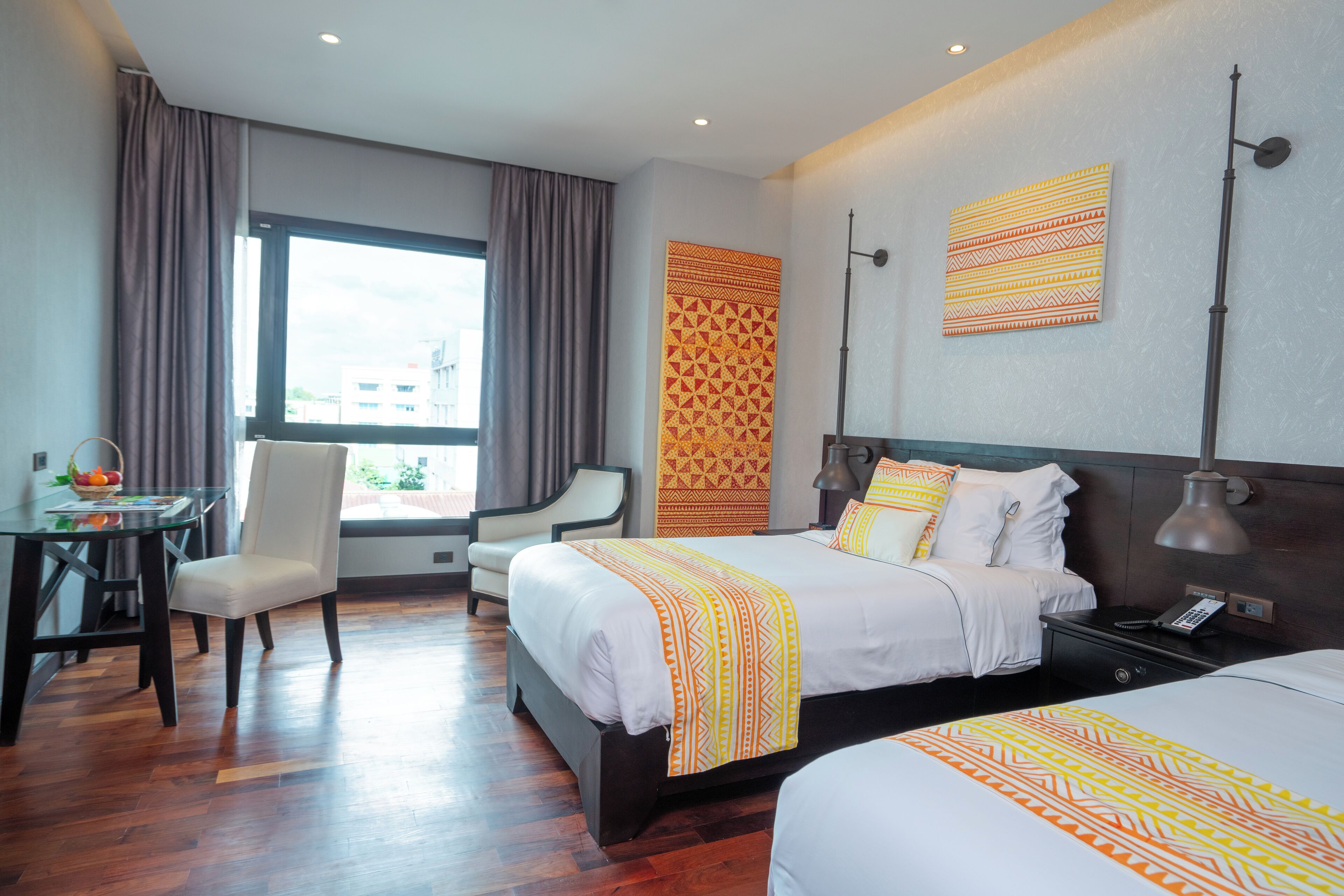 Una habitación de hotel con una cama grande, una cama más pequeña, un escritorio con una silla y una ventana con cortinas.