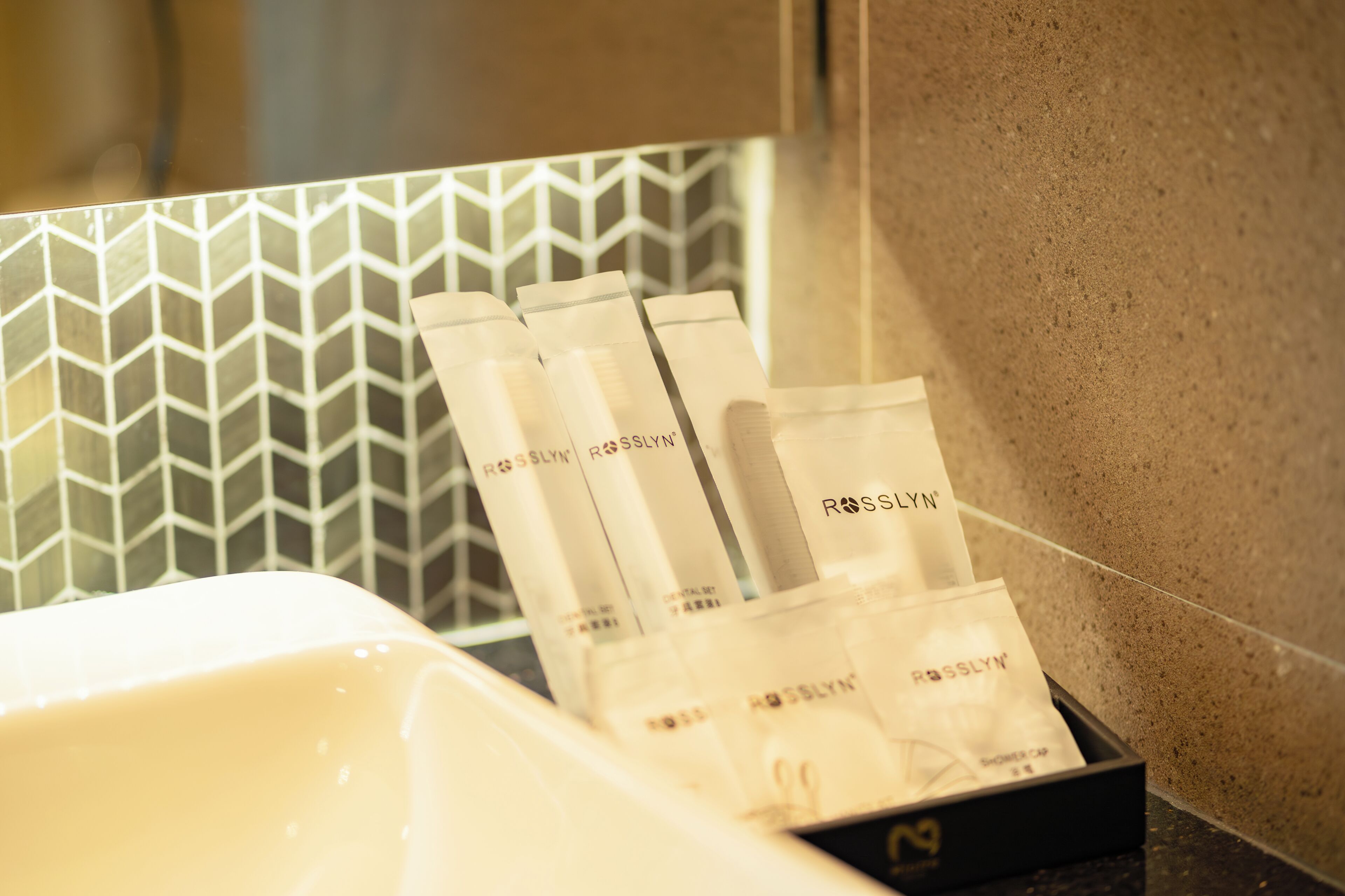 A bathroom with a white sink and a tray holding several bottles labeled 'ROSSLYN'.