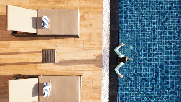 An aerial view of a poolside area with lounge chairs and a person swimming.