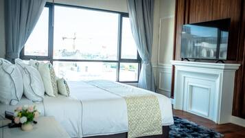 A hotel room with a large bed, a television, a fireplace, and a view of a building through the window.