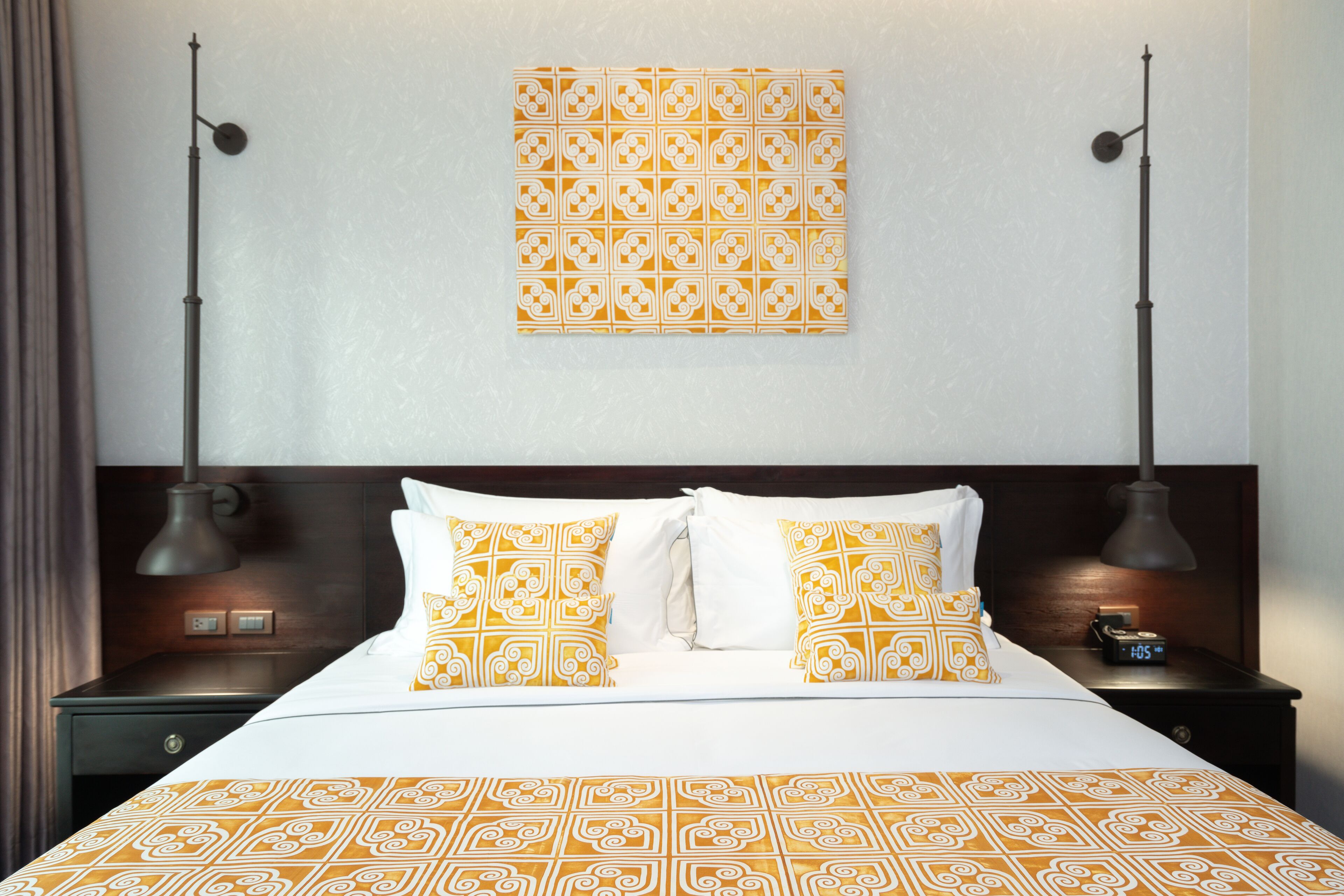 A neatly made bed with patterned pillows, a wall-mounted artwork, and two bedside lamps.
