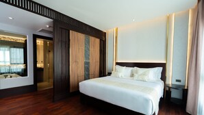 A modern hotel room with a large bed, wooden flooring, a walk-in closet, and a bathroom with a glass shower.