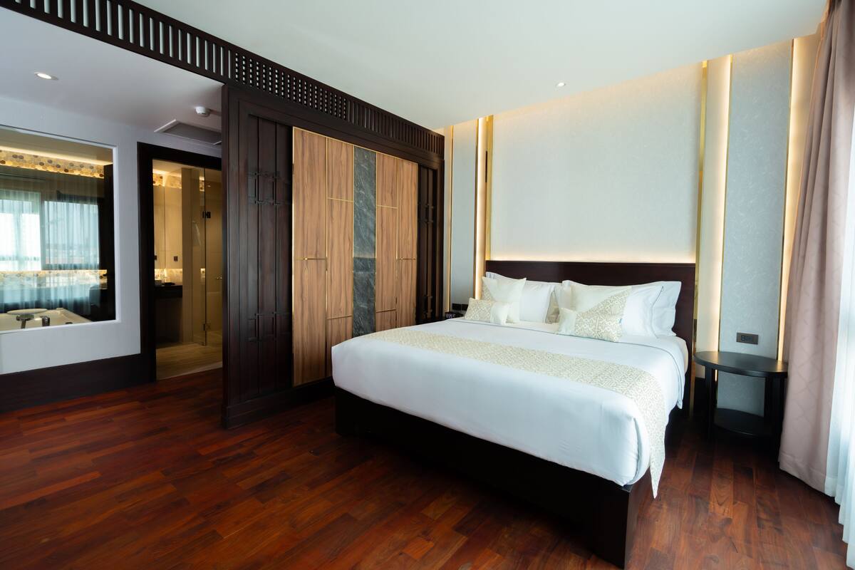 Une chambre d’hôtel moderne dotée d’un grand lit, d’un plancher en bois, d’un dressing et d’une salle de bain avec une douche en verre.