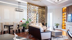 A modern living room with a sofa, dining table, and chairs. There is a decorative wall with a geometric pattern and a television on a stand.