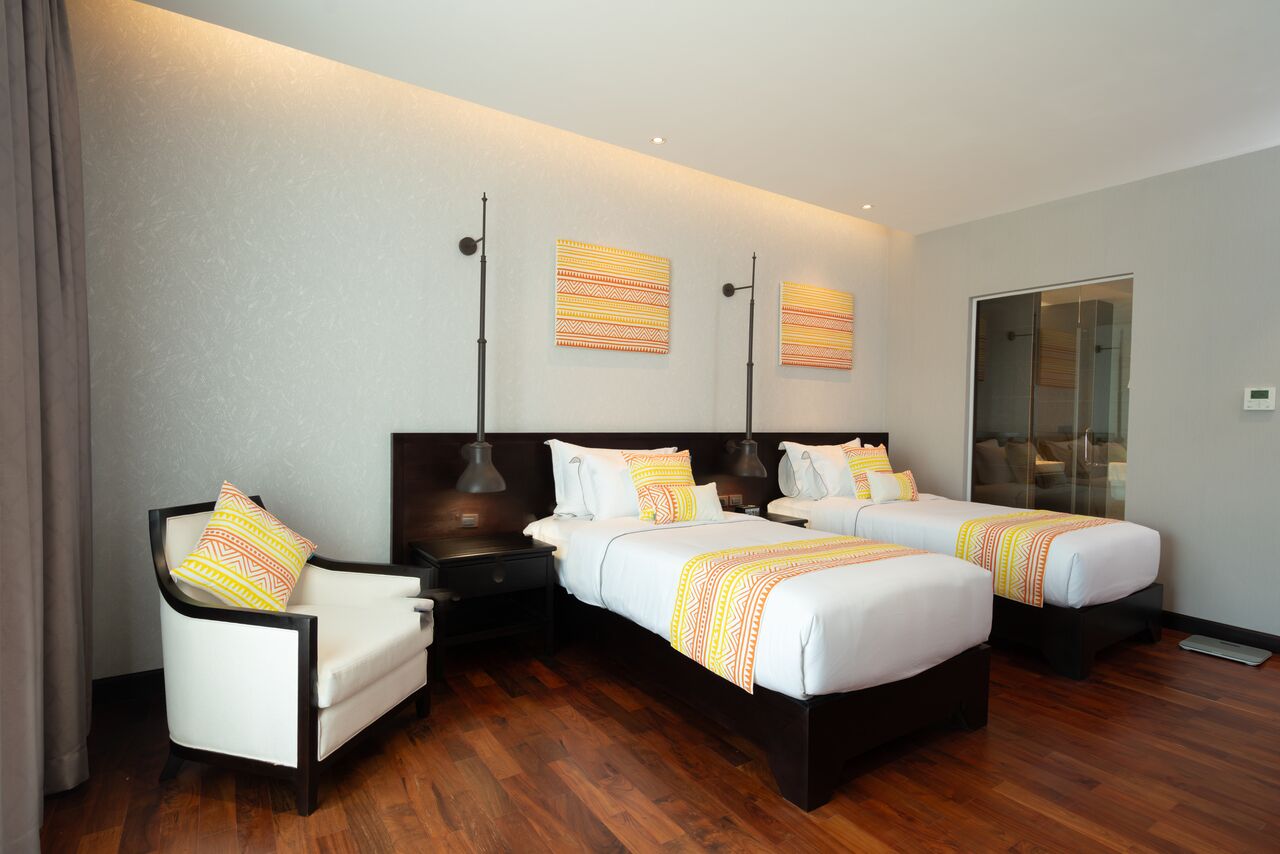 Quarto de hotel com duas camas, uma cadeira e uma mesa de cabeceira.