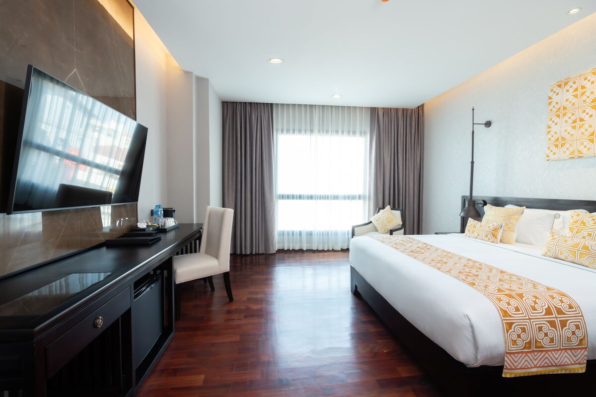 A hotel room with a bed, a desk, a chair, a TV, and a large window with curtains.