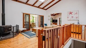 A spacious living area with a high ceiling, wooden beams, a fireplace, a dining area, and a balcony with a view.