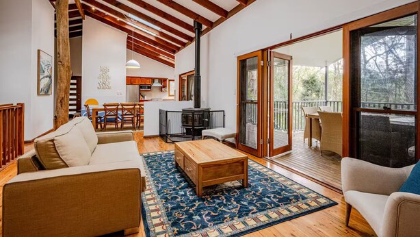 A spacious living area with a wooden ceiling, a dining table, and a kitchen in the background.