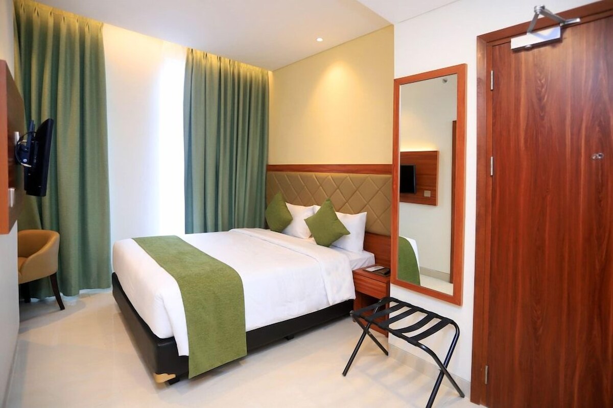 Una habitación de hotel con una cama, una silla, un escritorio, un espejo y una puerta.