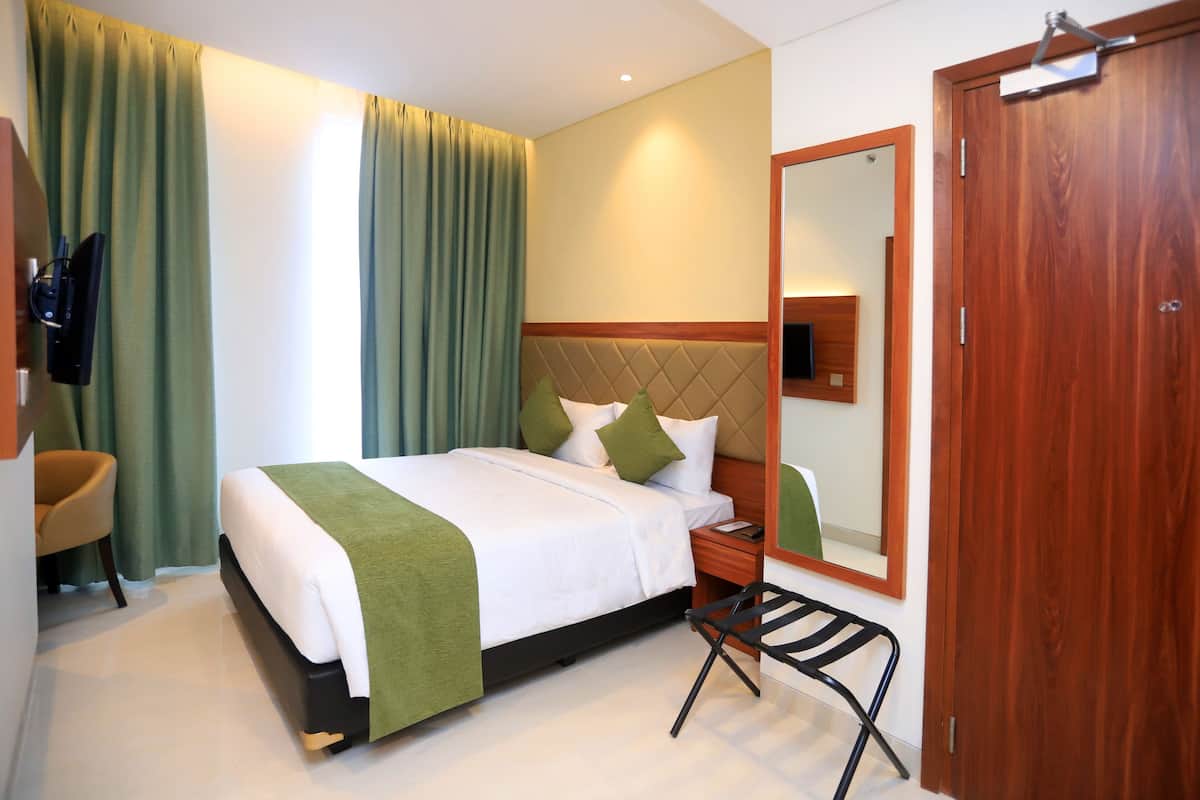 A hotel room with a bed, a chair, a nightstand, a mirror, and a door.