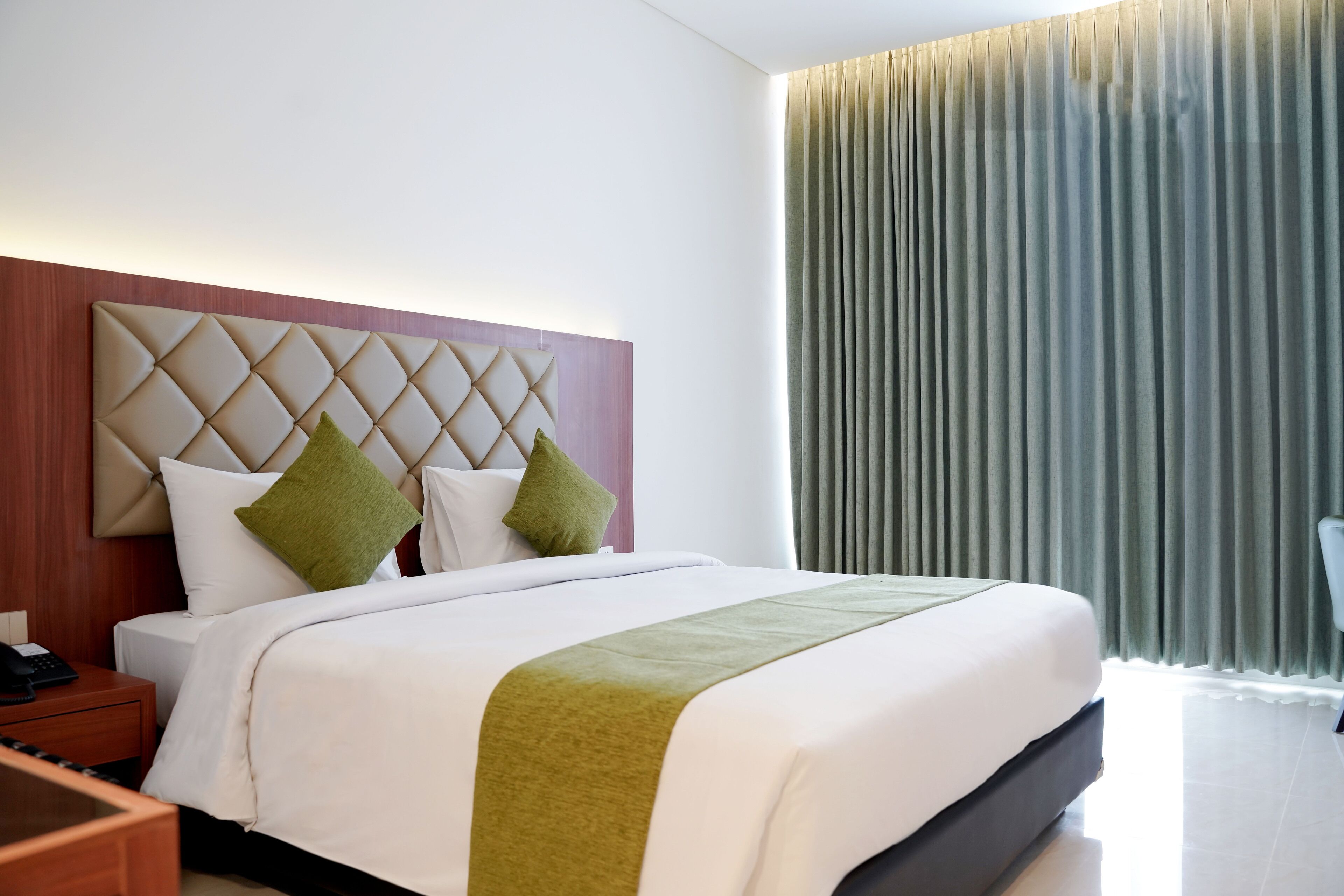Une chambre d’hôtel moderne avec un grand lit, une tête de lit en bois et un coussin décoratif vert.