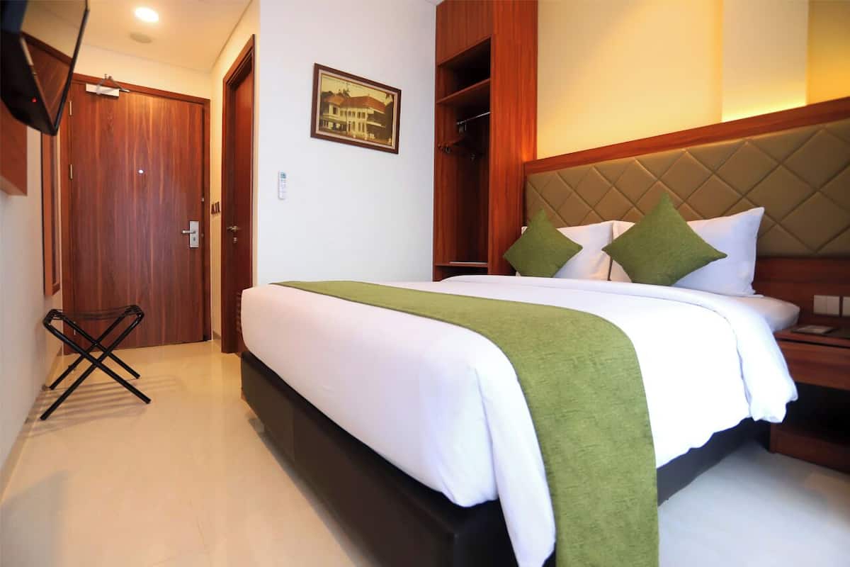 A hotel room with a large bed, a wooden wardrobe, a small table, and a picture on the wall.