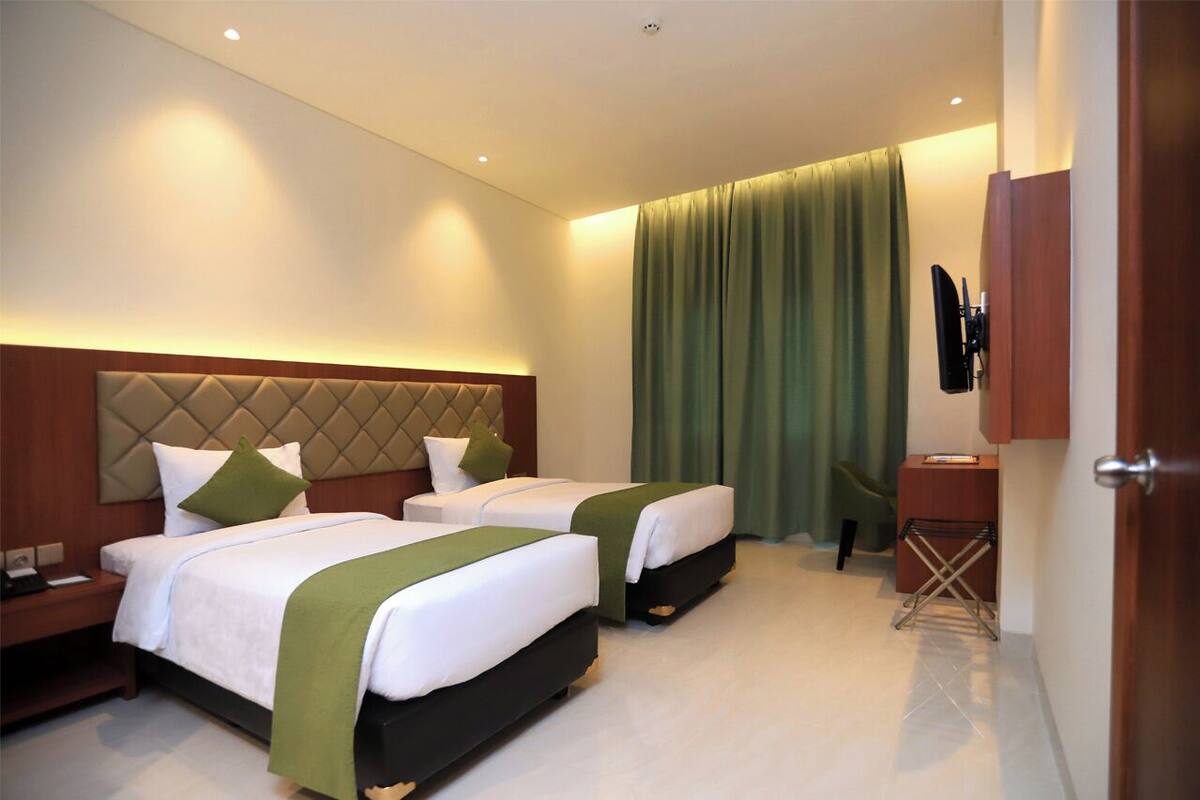 A hotel room with two beds, a desk, a chair, and a TV.