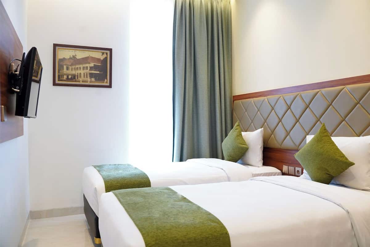 A hotel room with two beds, a mounted television, a framed picture on the wall, and a large window with curtains.