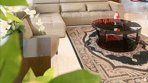 Een moderne woonkamer met een beige bank, een glazen salontafel en een kamerkleed met een patroon.
