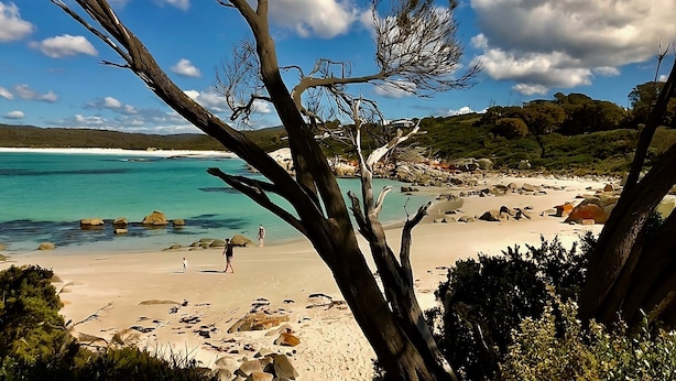 Una playa con agua turquesa cristalina, costa rocosa y algunas personas caminando.