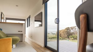 Un interior moderno con un puerta corrediza de vidrio que da a una terraza exterior, una silla verde y un diseño minimalista.