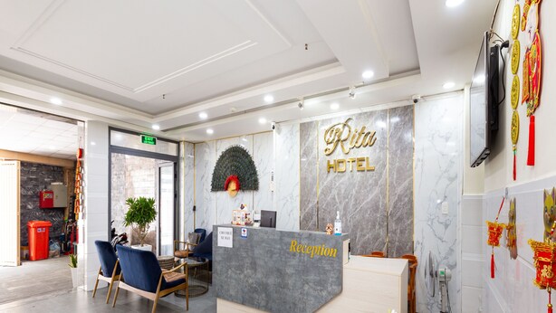A hotel reception area with a marble wall, a reception desk, and a seating area with chairs. - Rita Hotel (Ho Chi Minh City)