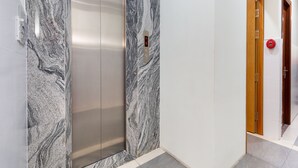 A modern elevator with marble walls and a digital display, a wooden door, and a red emergency button. - Rita Hotel (Ho Chi Minh City)