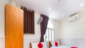 A hotel room with two wooden beds, a small wooden table, a window with curtains, an air conditioning unit, and a wall-mounted fan. - Rita Hotel (Ho Chi Minh City)