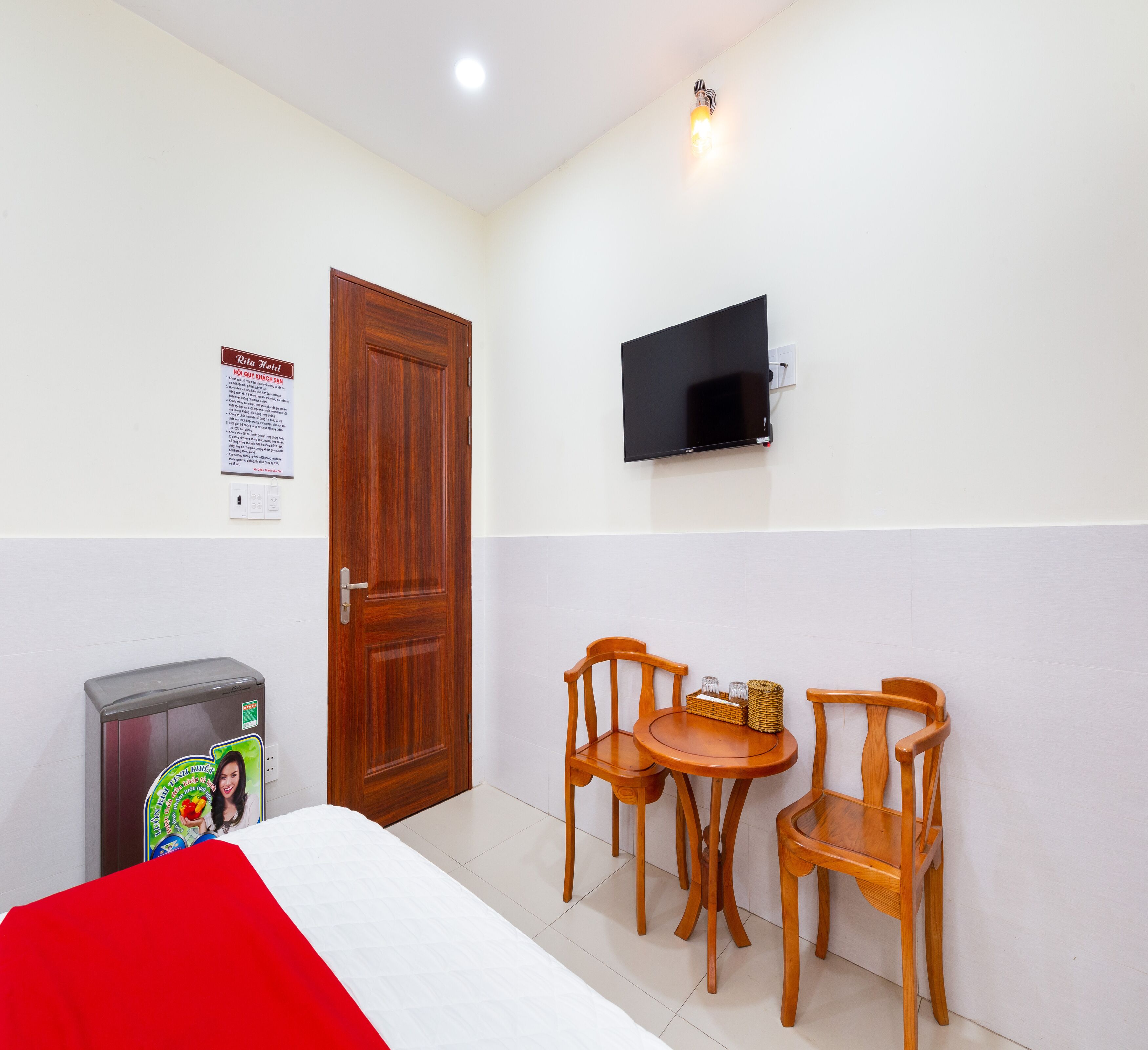 Habitación de hotel con cama, televisor montado en la pared y dos sillas de madera alrededor de una mesita.